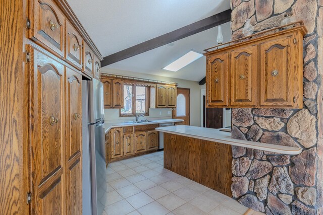 kitchen with stainless steel appliances, brown cabinets, a skylight, light tile patterned flooring, and light countertops