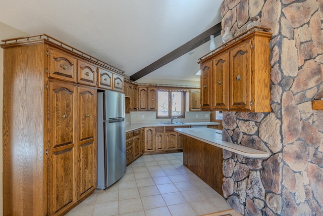 kitchen featuring freestanding refrigerator, brown cabinets, a sink, light countertops, and beamed ceiling