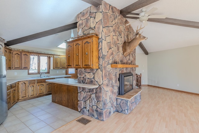 kitchen featuring beamed ceiling, brown cabinets, light countertops, freestanding refrigerator, and a sink