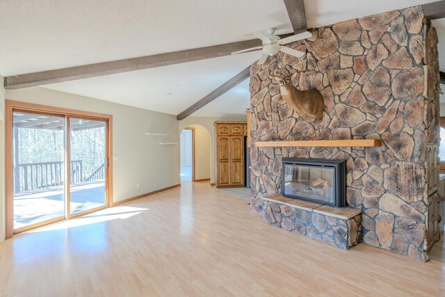 unfurnished living room with ceiling fan, arched walkways, light wood-style flooring, baseboards, and a stone fireplace