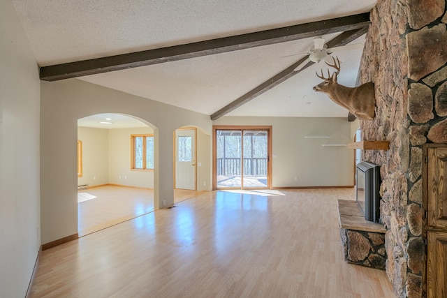 unfurnished living room featuring a ceiling fan, baseboards, light wood-style flooring, arched walkways, and a textured ceiling