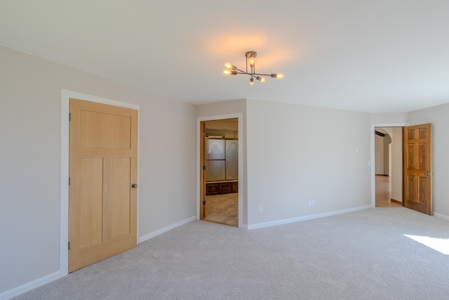 unfurnished bedroom featuring light colored carpet, a chandelier, and baseboards