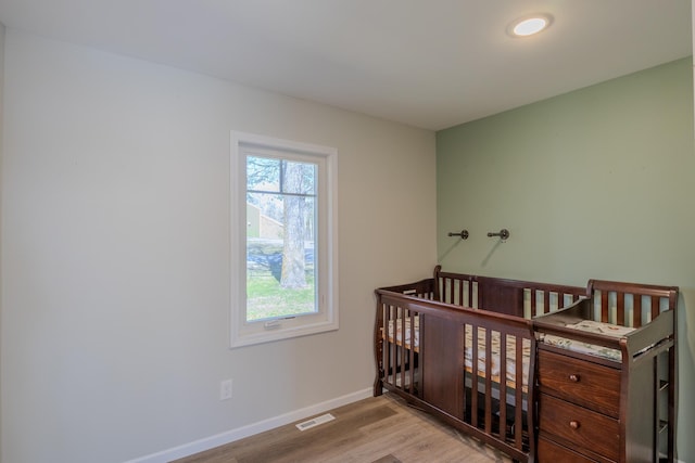 bedroom with wood finished floors, baseboards, and a crib