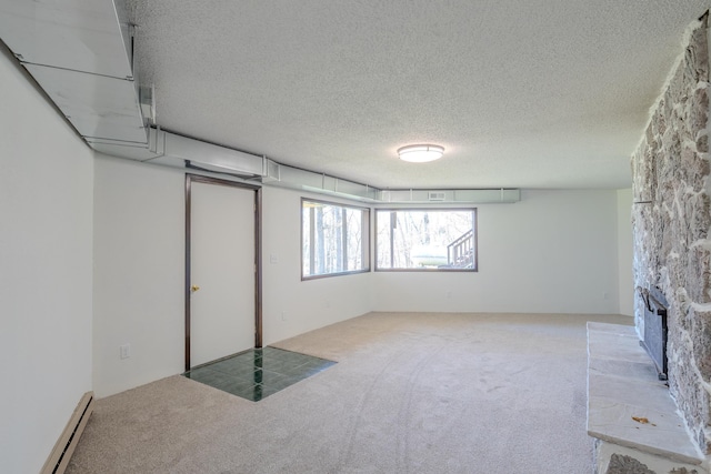 below grade area with a baseboard radiator, carpet, a textured ceiling, and a stone fireplace