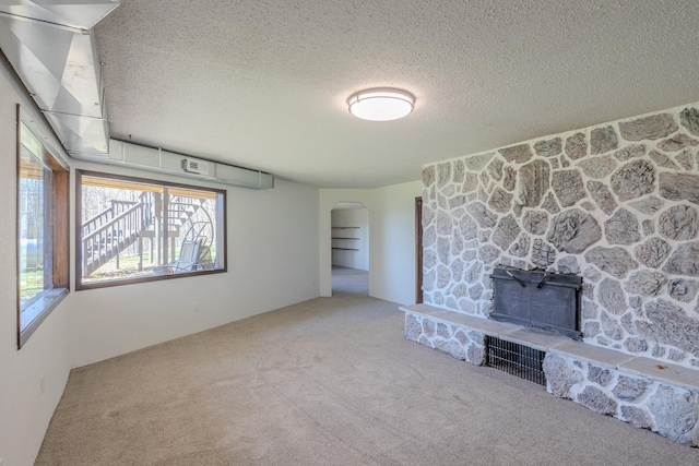 unfurnished living room with arched walkways, carpet flooring, and a textured ceiling