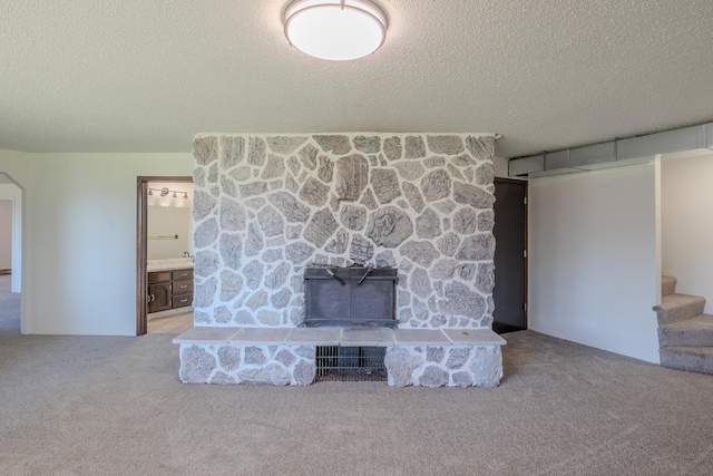 unfurnished living room with carpet, a textured ceiling, stairway, arched walkways, and a fireplace