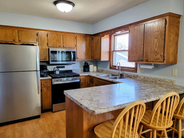 kitchen with appliances with stainless steel finishes, a sink, a peninsula, brown cabinetry, and a textured ceiling