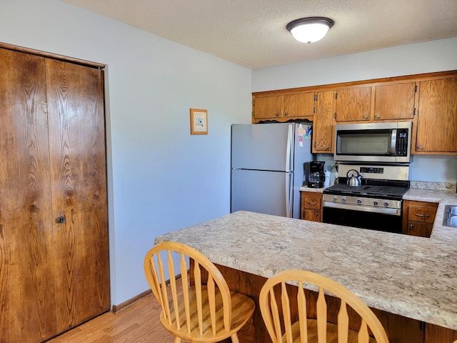kitchen with appliances with stainless steel finishes, light countertops, light wood-type flooring, brown cabinetry, and a kitchen bar