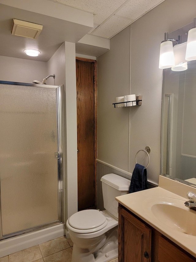 bathroom with a stall shower, tile patterned floors, vanity, toilet, and a wainscoted wall