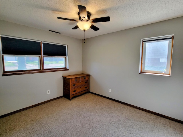 unfurnished room featuring healthy amount of natural light, light carpet, a ceiling fan, and a textured ceiling