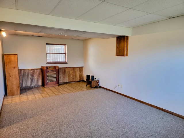 basement featuring a drop ceiling, light colored carpet, and baseboards