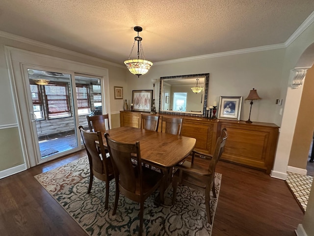 dining area featuring dark wood-type flooring, a textured ceiling, arched walkways, ornamental molding, and baseboards