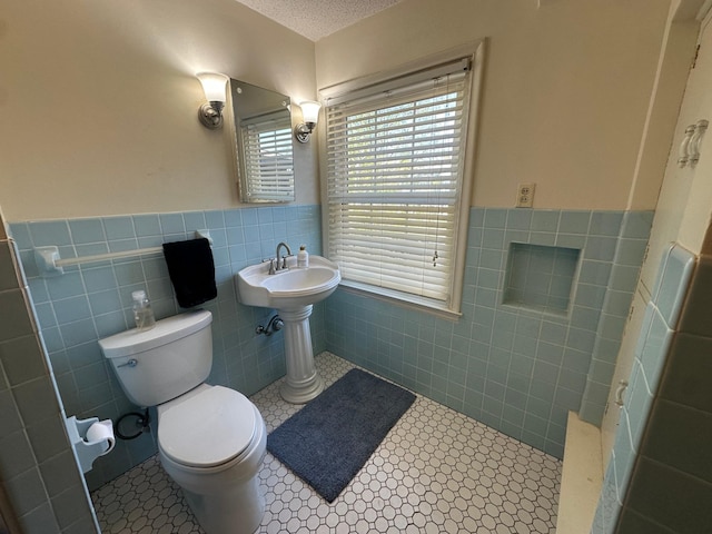full bath with tile walls, wainscoting, toilet, a textured ceiling, and tile patterned floors