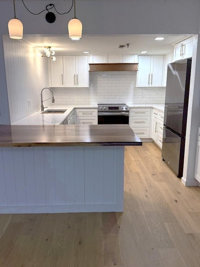 kitchen with appliances with stainless steel finishes, a sink, a peninsula, white cabinets, and backsplash