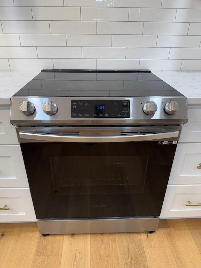 kitchen view of electric stove, white cabinetry, light countertops, and decorative backsplash