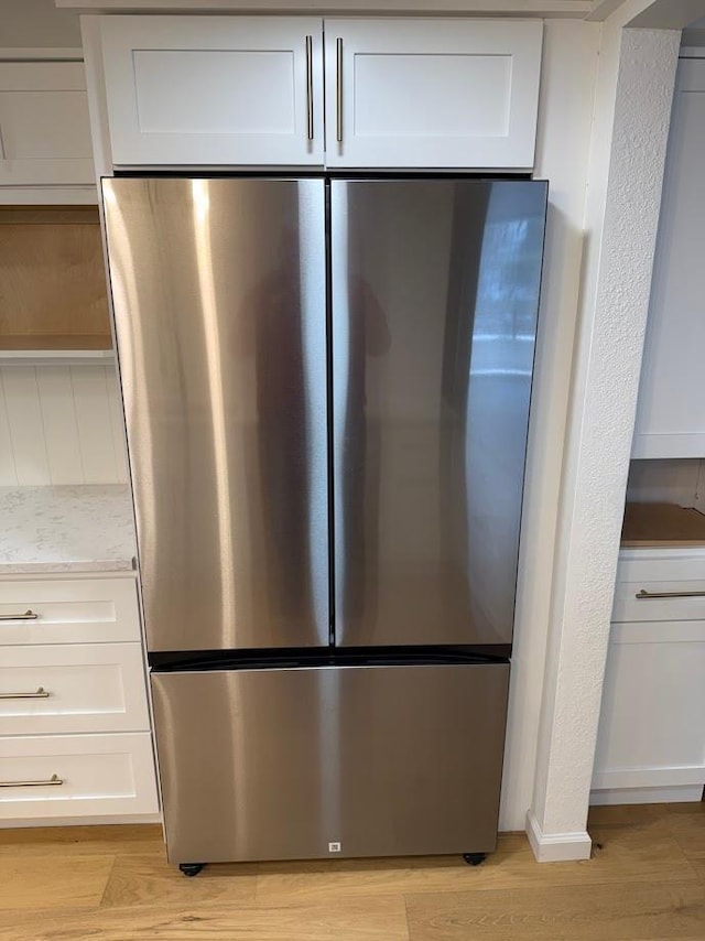 kitchen view of freestanding refrigerator, light wood-type flooring, white cabinets, light stone counters, and open shelves