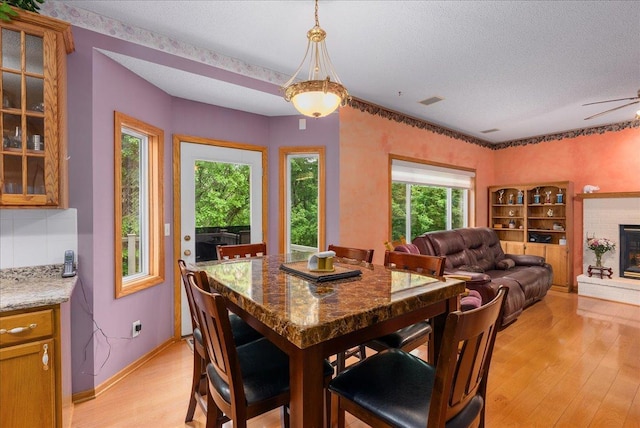9230 Cheney Trl, Inver Grove Heights, MN 55076 - dining space with light wood finished floors, a textured ceiling, a brick fireplace, a ceiling fan, and baseboards