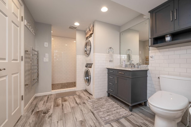 full bath with estacked washer and dryer, tile walls, toilet, a walk in shower, and wood finished floors