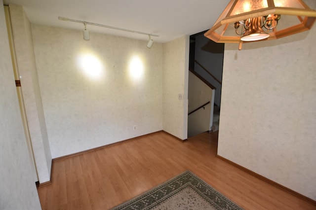 empty room featuring rail lighting, wood finished floors, and baseboards