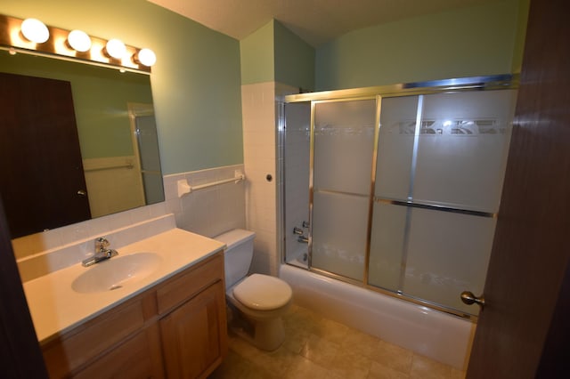 bathroom with toilet, shower / bath combination with glass door, vanity, tile patterned flooring, and tile walls