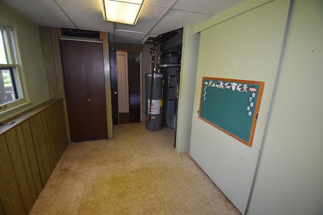 hall with gas water heater, light flooring, and a paneled ceiling