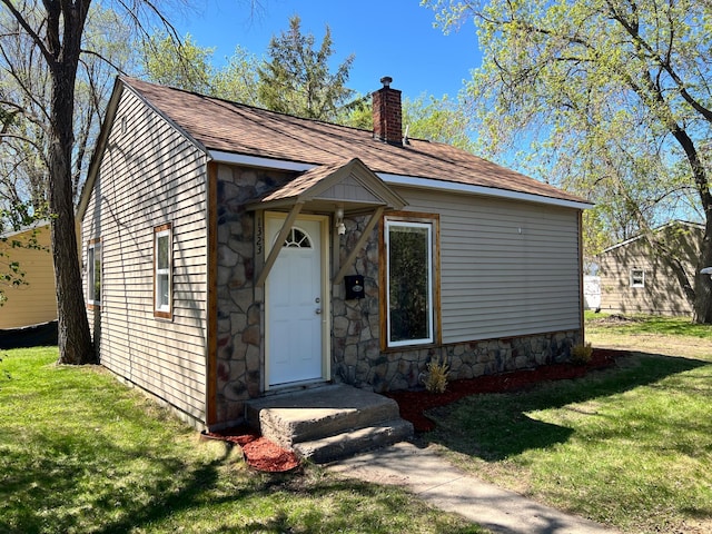 view of front of property featuring stone siding, a chimney, a front lawn, and roof with shingles