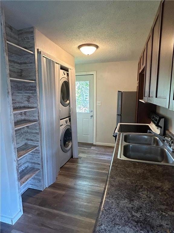 washroom with stacked washer / drying machine, dark wood finished floors, a textured ceiling, and baseboards