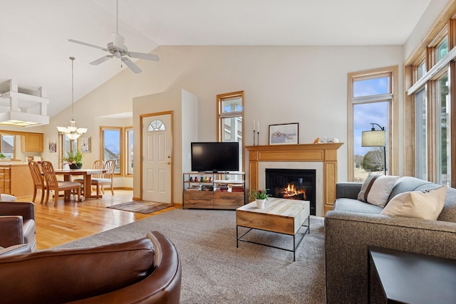 living room featuring healthy amount of natural light, a glass covered fireplace, a chandelier, wood finished floors, and high vaulted ceiling