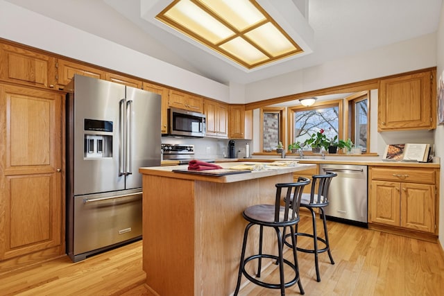 kitchen featuring stainless steel appliances, light wood-style floors, lofted ceiling, a kitchen island, and a breakfast bar