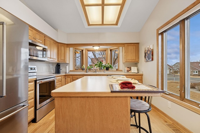 kitchen featuring stainless steel appliances, light wood-style flooring, a kitchen bar, light countertops, and a center island