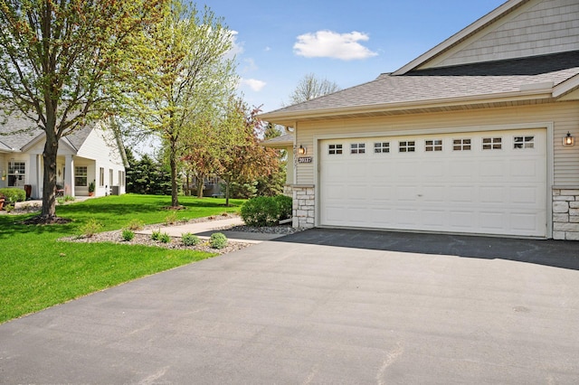 view of side of property featuring stone siding, a shingled roof, asphalt driveway, and a yard