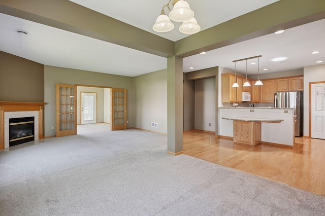 unfurnished living room with light carpet, recessed lighting, a chandelier, baseboards, and a fireplace