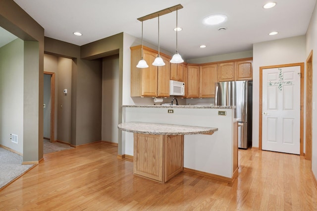 kitchen featuring white microwave, freestanding refrigerator, light wood finished floors, light stone counters, and baseboards