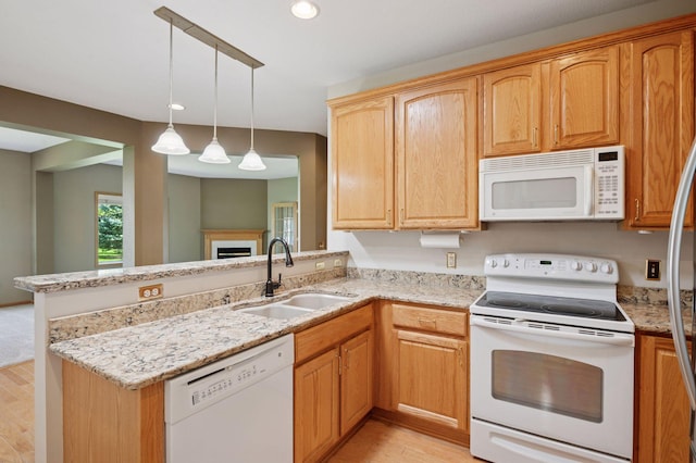 kitchen with white appliances, a sink, light wood finished floors, a peninsula, and light stone counters