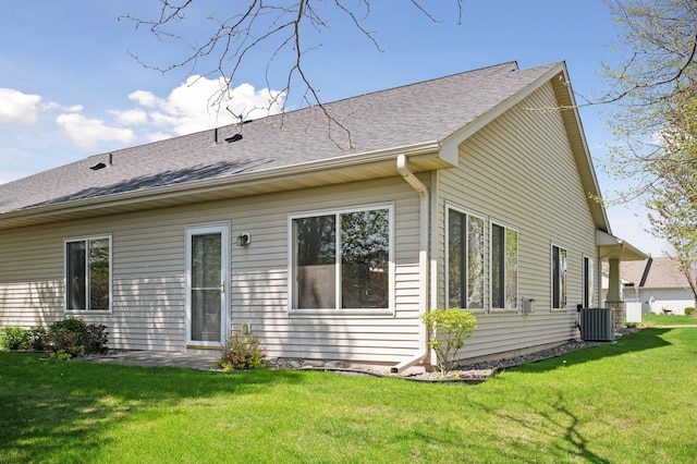 back of property featuring central air condition unit, a lawn, and roof with shingles