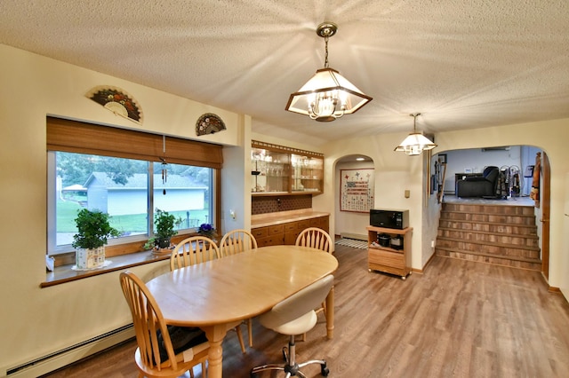 1300 10th St NE, Sauk Rapids Twp, MN 56379 - dining space featuring arched walkways, baseboard heating, light wood-type flooring, a chandelier, and a textured ceiling