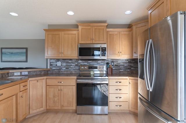 kitchen with appliances with stainless steel finishes, light brown cabinets, dark countertops, light wood-type flooring, and recessed lighting