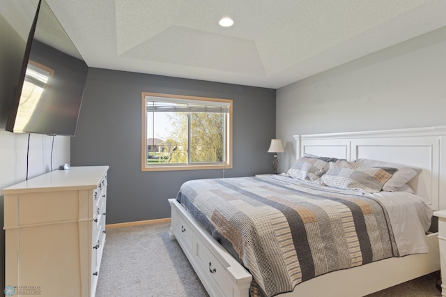 bedroom featuring light colored carpet, a tray ceiling, and baseboards