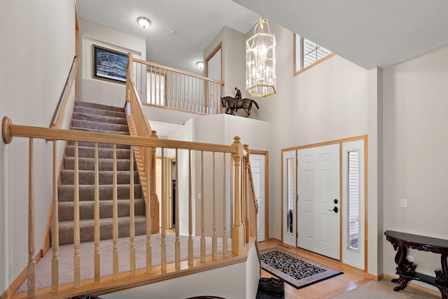 foyer entrance featuring stairway, a chandelier, wood finished floors, a towering ceiling, and baseboards