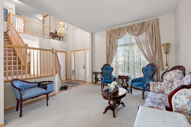 living area featuring a chandelier, carpet floors, stairway, a towering ceiling, and baseboards