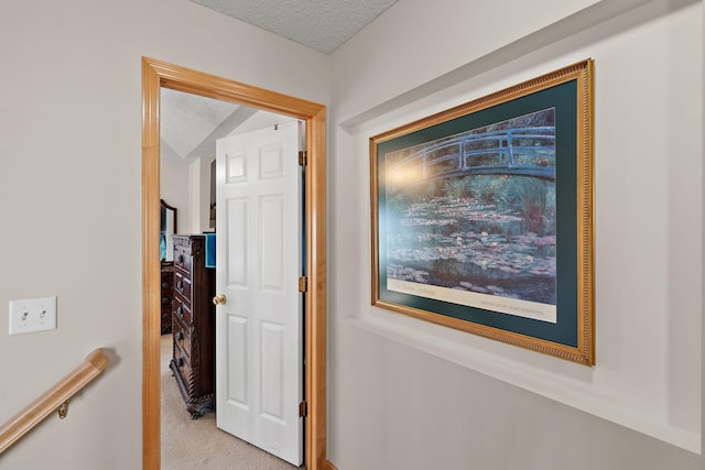 corridor with a textured ceiling, light colored carpet, and an upstairs landing