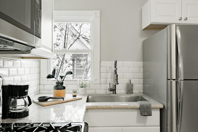 1541 Charles Ave, Saint Paul, MN 55104 - kitchen featuring appliances with stainless steel finishes, a sink, backsplash, white cabinetry, and light stone counters
