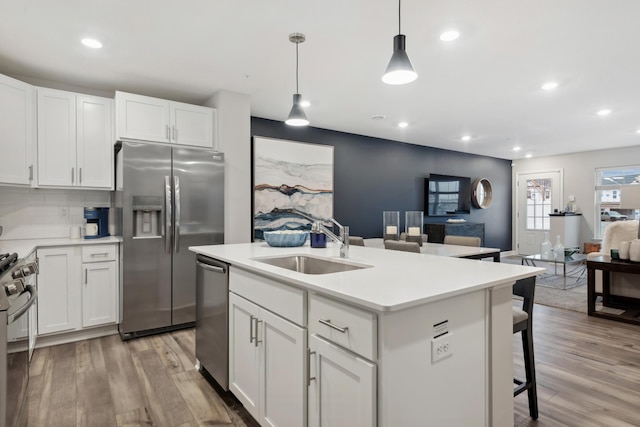 kitchen with stainless steel appliances, a sink, open floor plan, light wood finished floors, and light countertops