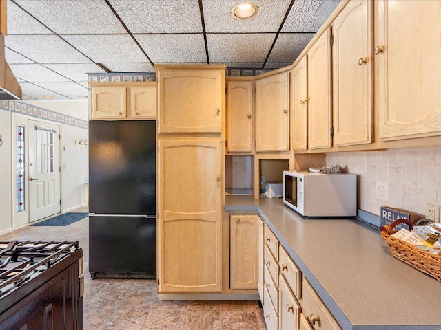 kitchen with freestanding refrigerator, white microwave, light brown cabinetry, a drop ceiling, and decorative backsplash