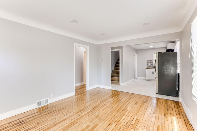 spare room featuring stairs, light wood-style flooring, baseboards, and a sink