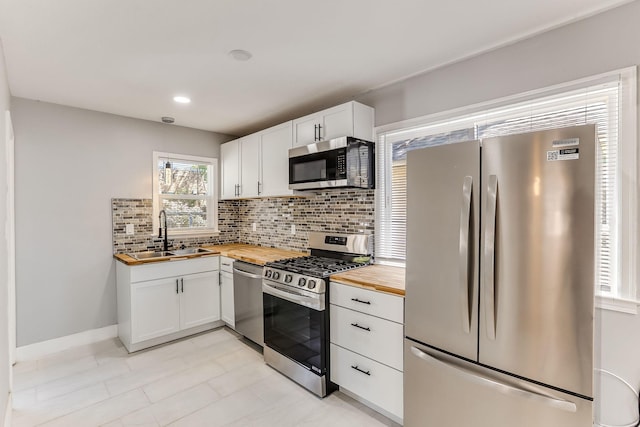 kitchen featuring stainless steel appliances, butcher block countertops, a sink, decorative backsplash, and white cabinets