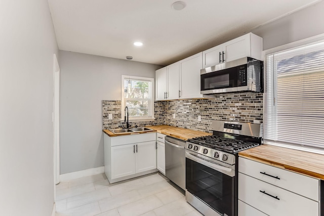 kitchen featuring appliances with stainless steel finishes, wood counters, a sink, decorative backsplash, and white cabinets