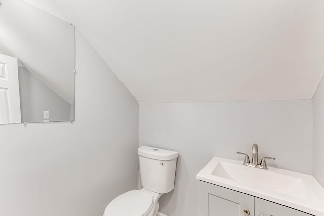 half bathroom with vaulted ceiling, toilet, and vanity