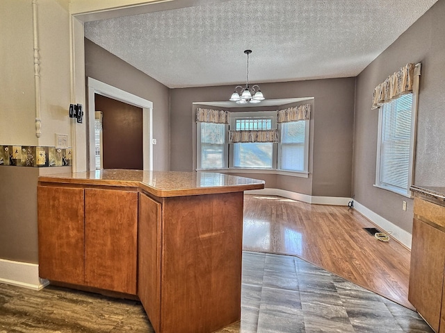 1501 Park St, Fairmont, MN 56031 - kitchen featuring plenty of natural light, a chandelier, a textured ceiling, brown cabinetry, and a peninsula
