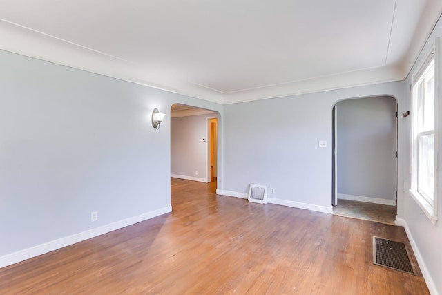 unfurnished room with arched walkways, wood finished floors, and baseboards